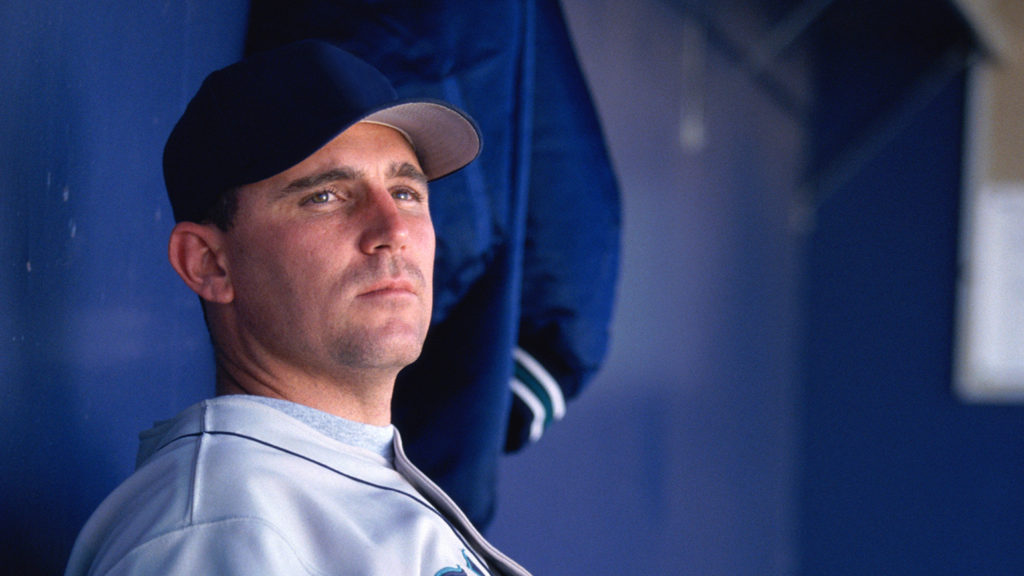 A lone baseball player looks on from the dugout as his teammates play the game 