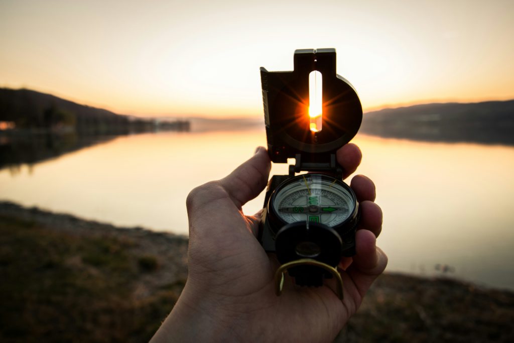 A hand holds a compass over the water at sunset showing how to navigate offenses by building resilience.