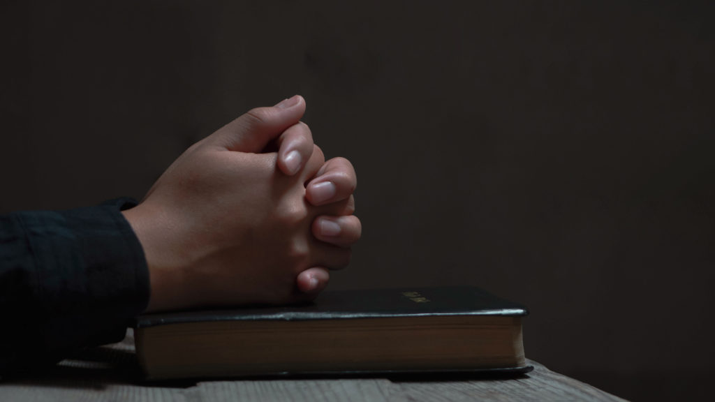 Hands clasped in prayer on a Bible in the dark for when you can't sleep.