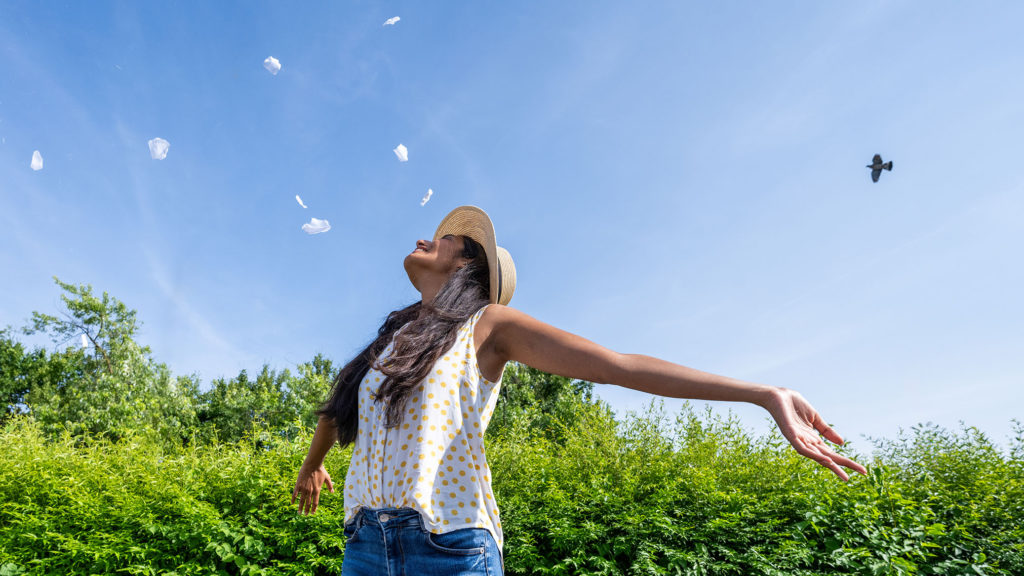 A young woman with wide open arms outside on a sunny day has learned to choose contentment.