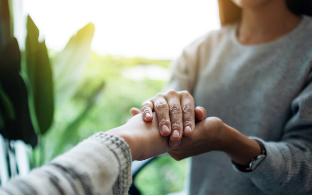 A woman holds another woman's hand in both of hers to gain emotional stability.