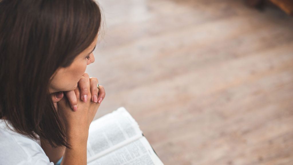 A yong woman prays with an open Bible as she seeks to understand the difference between faith and doubt.