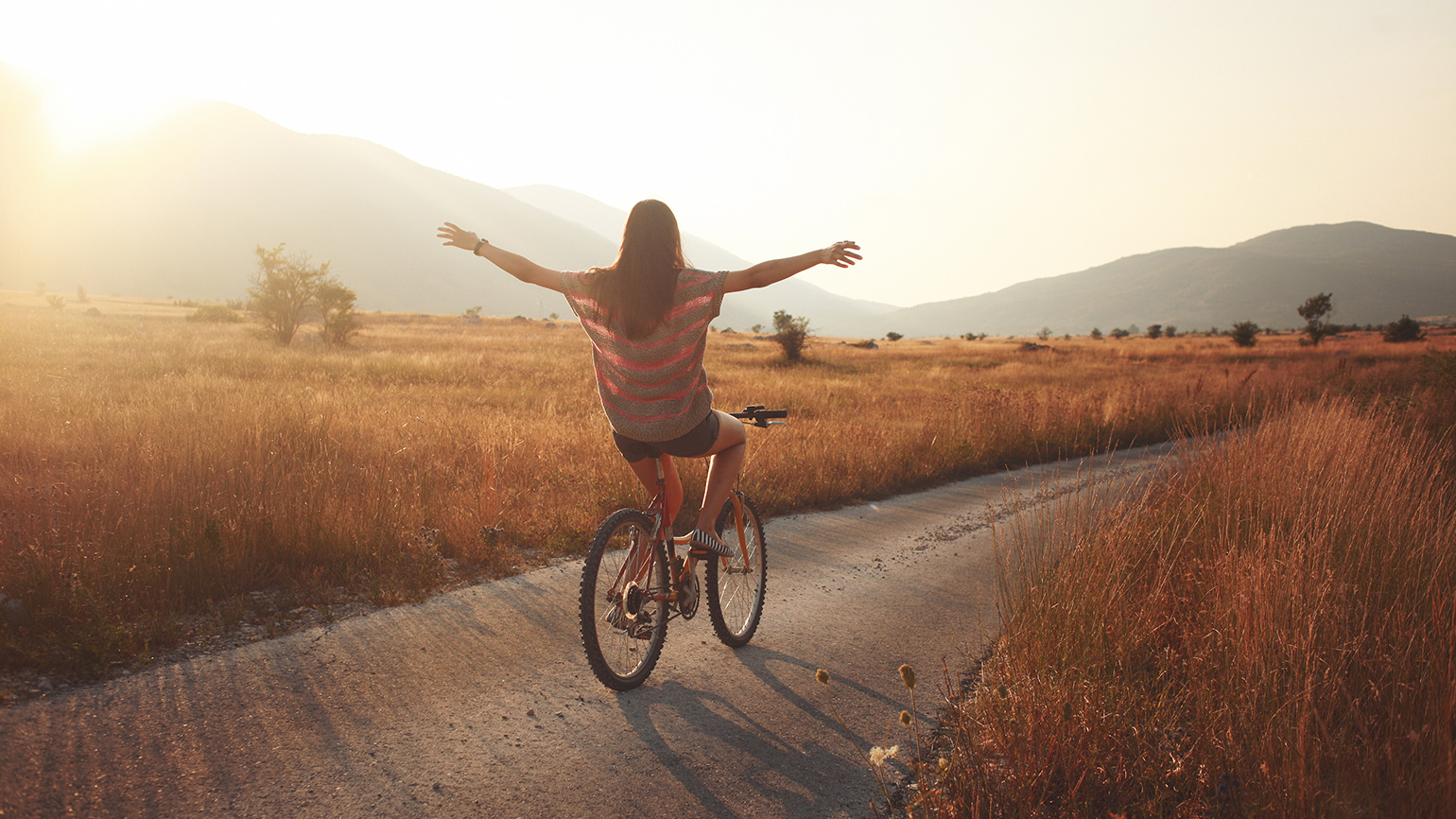 Royalty-Free Stock Photo: Young woman finding joy by riding a bike at sunset.
