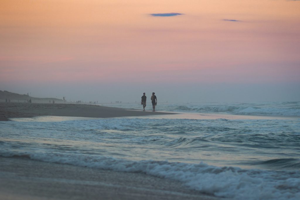 Two people walk on the beach at sunset learning how to become unoffendable.