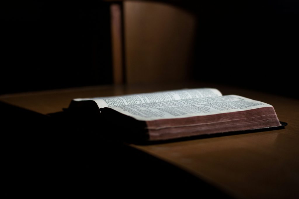 An open Bible on a dark wood desk offers wisdom for living above offense.