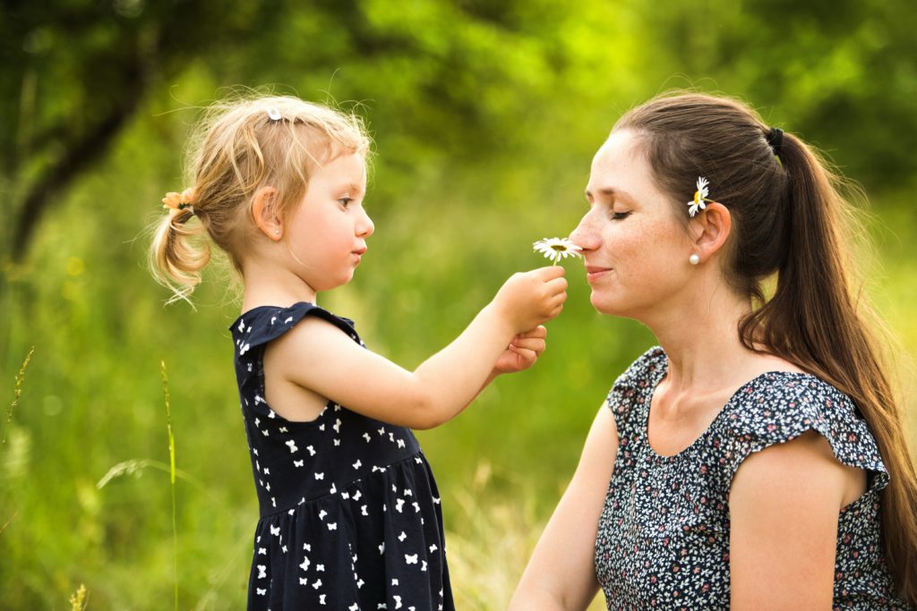 A small girl hold a flower up to her mom's nose knowing that she is more than enough as God's beloved child.