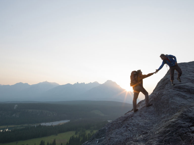 One climber helps another up a steep rock during sunset knowing this helps you claim your confidence.