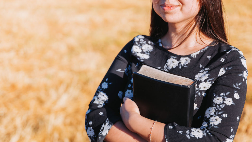 A young woman holds a black Bible to her chest where she has found the answer to the question, "What is contentment?"