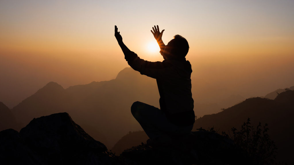 A man lifts his hands to God in prayer on a mountain at sunset when he wants to question God about some doubt he has.