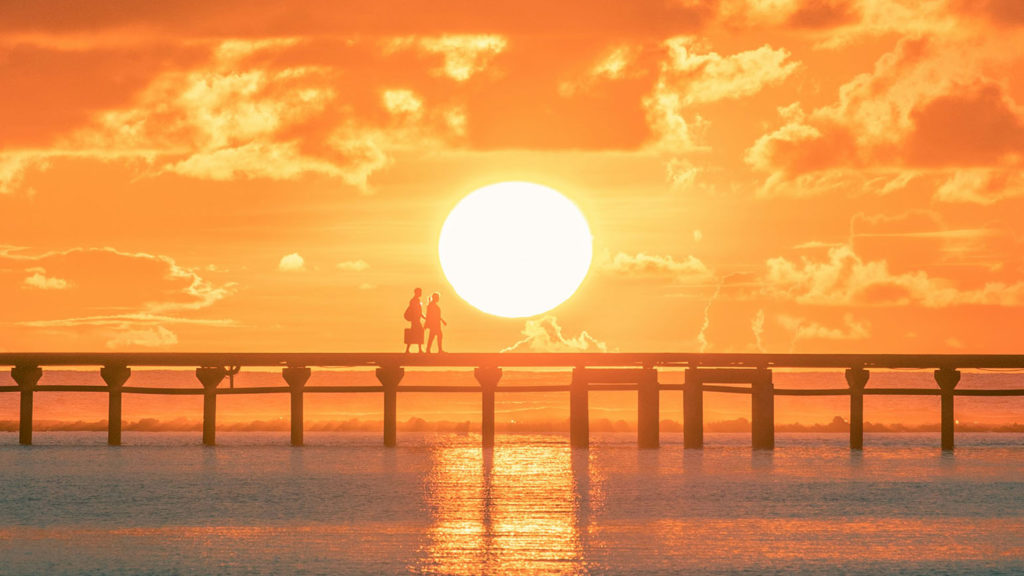 Two people walk on a pier in front of a brilliant sunset as they show you how to give Jesus your baggage and live at peace.
