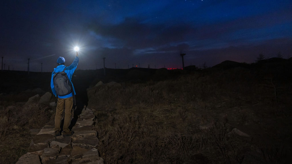 A lone hiker holds up a light reminding him of God's light in the darkness.