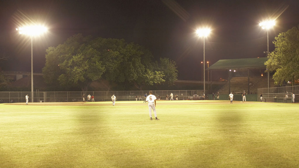 Baseball players on the field under bright lights like from classic baseball movies.