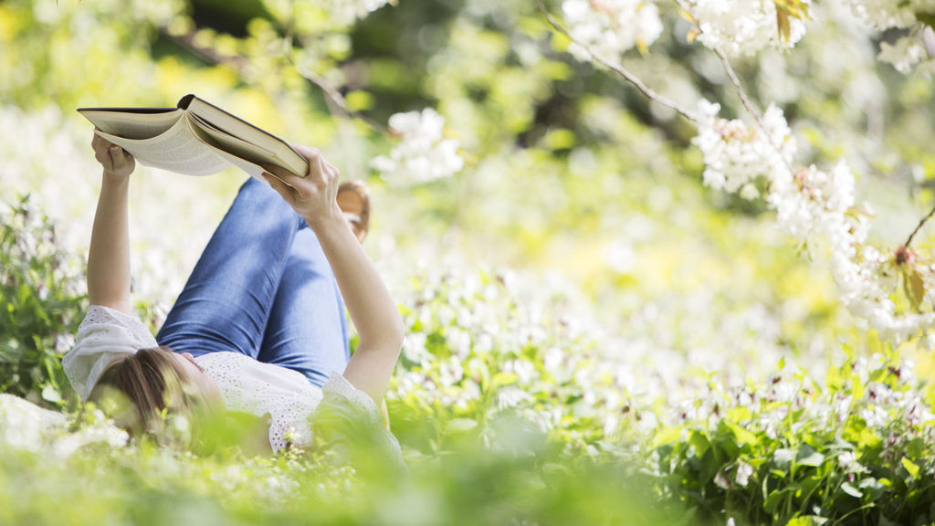 A woman lies on her back amongst white flowers reading the Bible to keep from becoming a fair-weather fan.