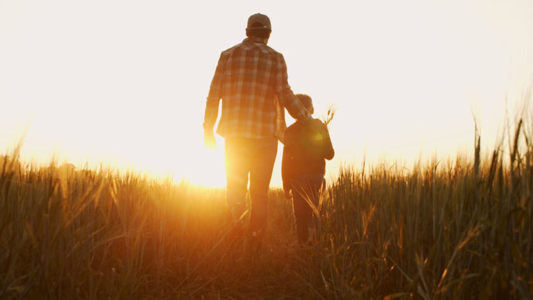 A boy walkd in a field at sunset confident in his father's delight in him.