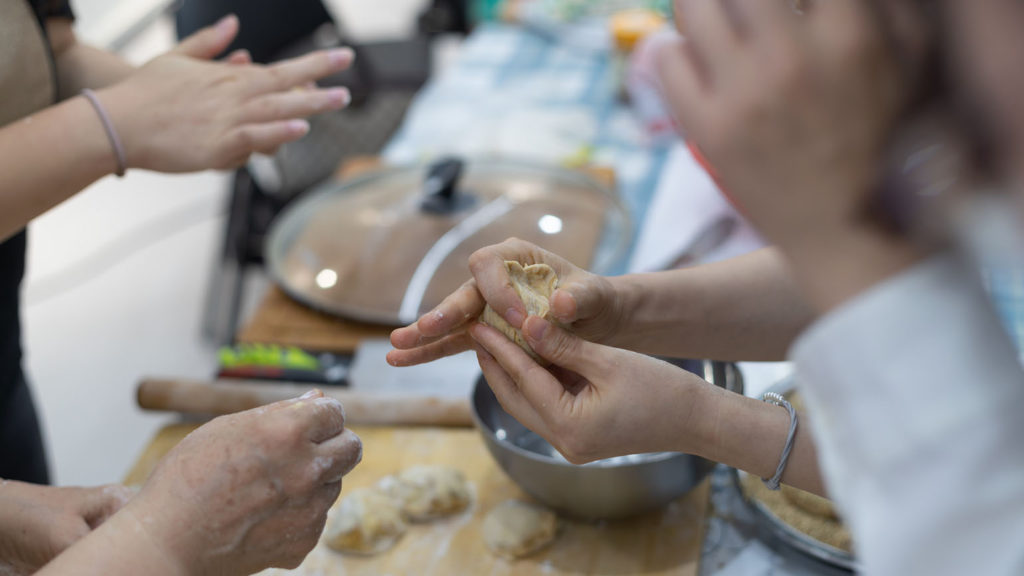 Hands forming dough show friends enjoying the fellowship of cooking together.