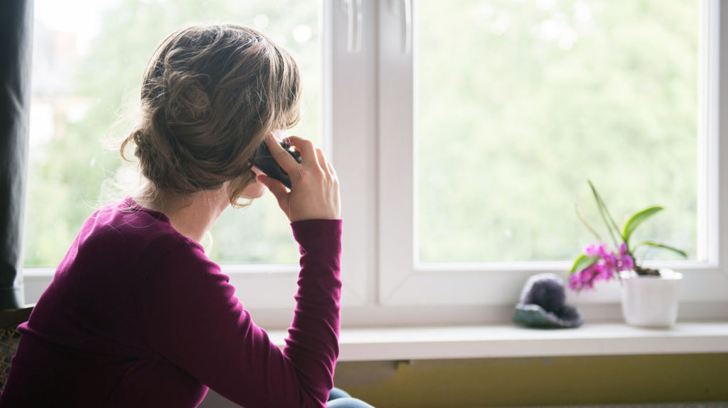 A woman in a purple shirt gazes out the window as she talks on the phone with a friend who needs to see love in action.