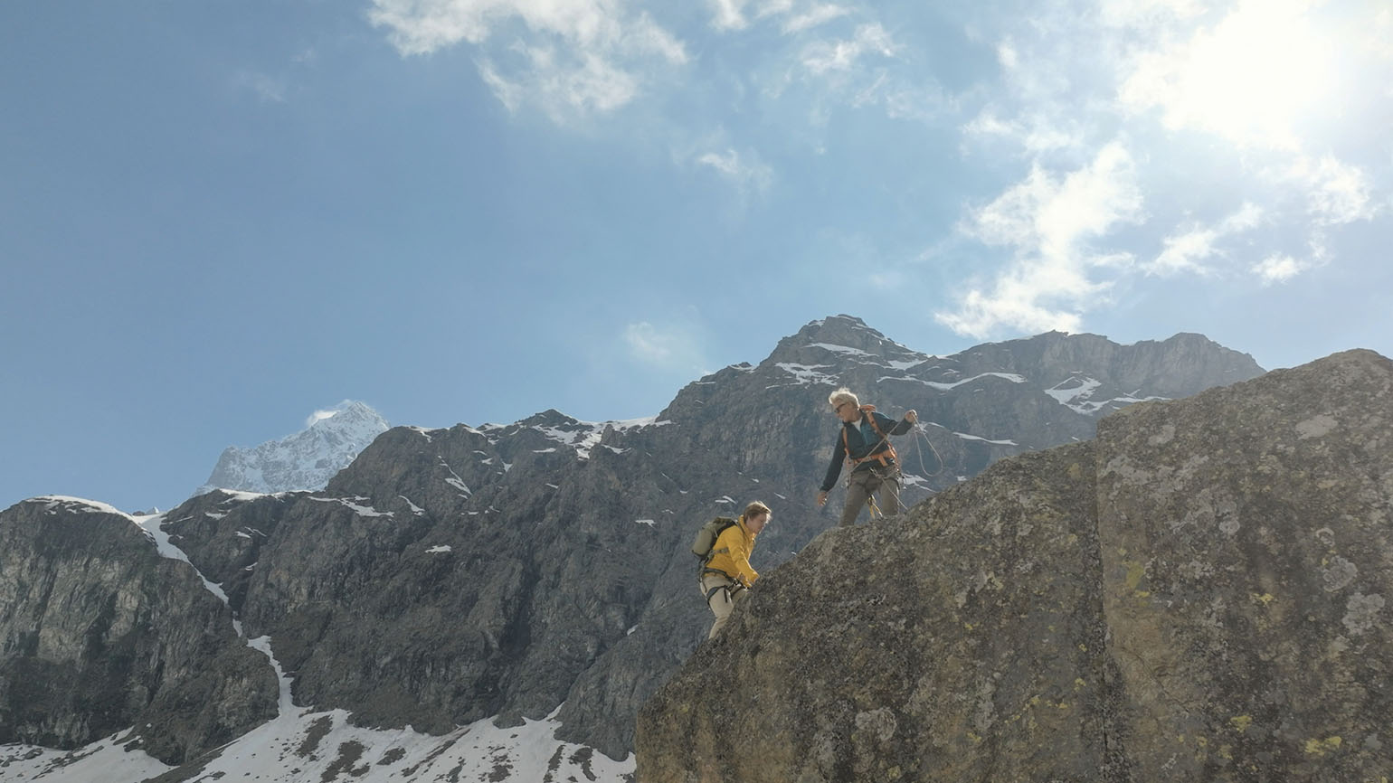 Two hikers on a mountain on a clear day strengthen bonds by helping each other.