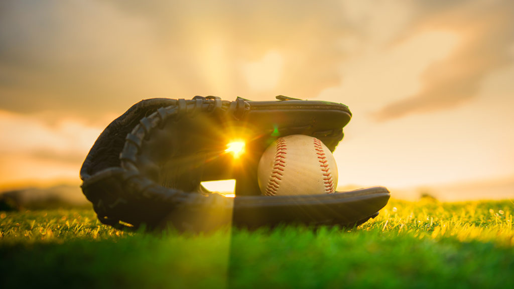 Royalty-Free Stock Photo: Baseball in a glove on grass at sunset depicting how to understand faith through baseball.