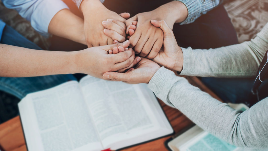 Royalty-Free Stock Photo: Christian friends joining hands and praying together over bible on wooden table.