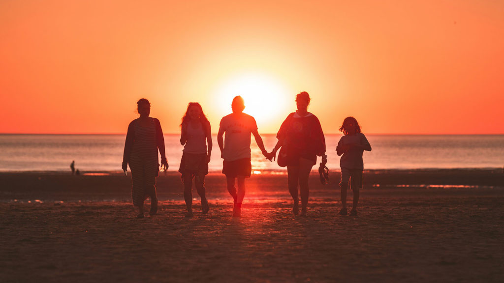 5 friends in silhouette walk on the beach toward the sunset showing the beauty of worshipping together.