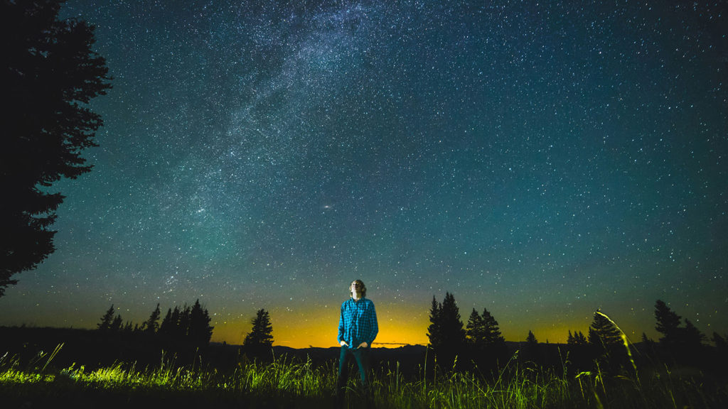A young man stands outside gazing at the dark sky full of stars as he practices Christian evening meditation.