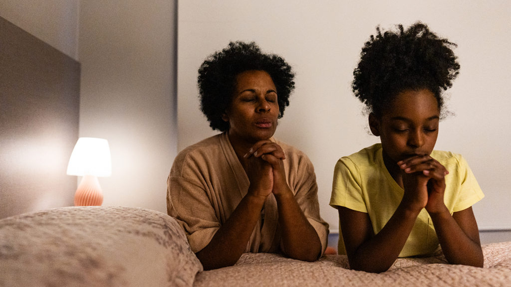 Mother and daughter say their bedtime prayers at their bed