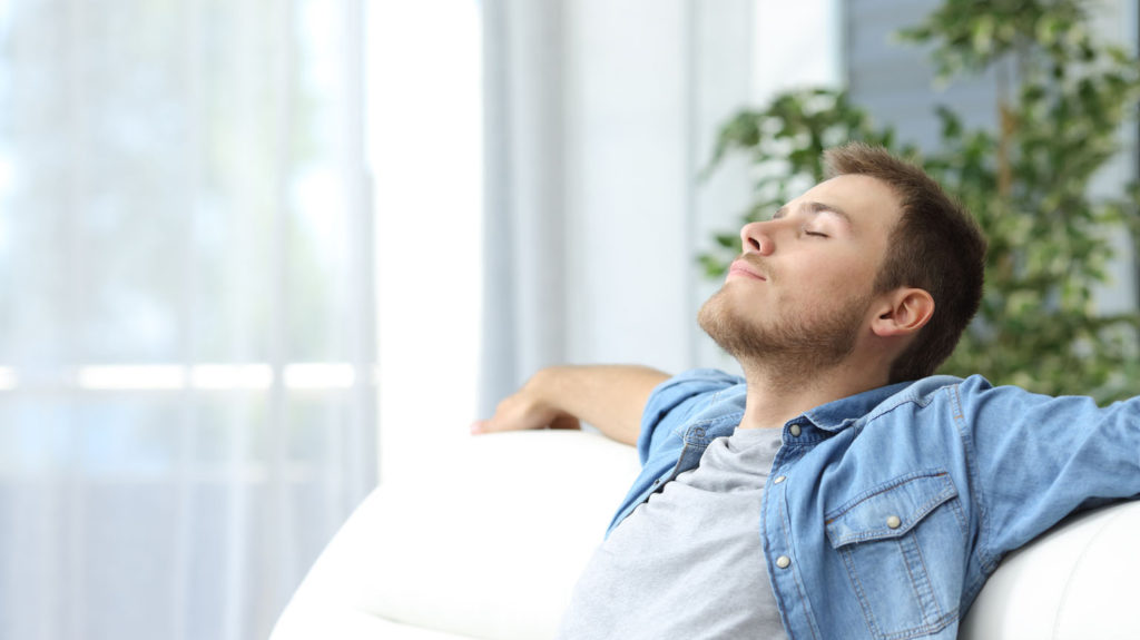 A young man sits peacefully on his couch with his eyes closed as he learns about calming your mind.