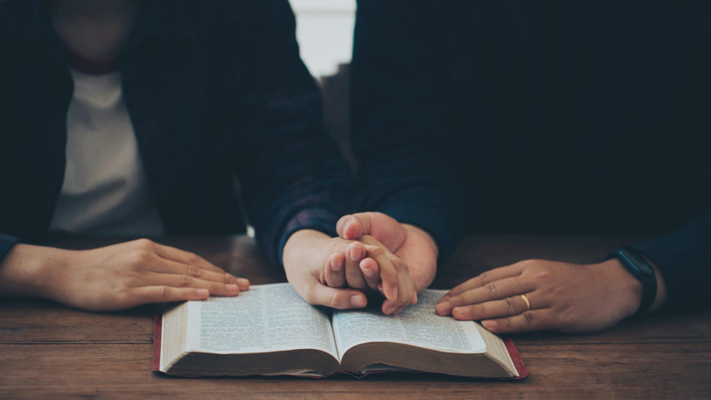 Royalty-Free Stock Photo: Man and woman holding hands over a Bible and doing night prayers for couples. 