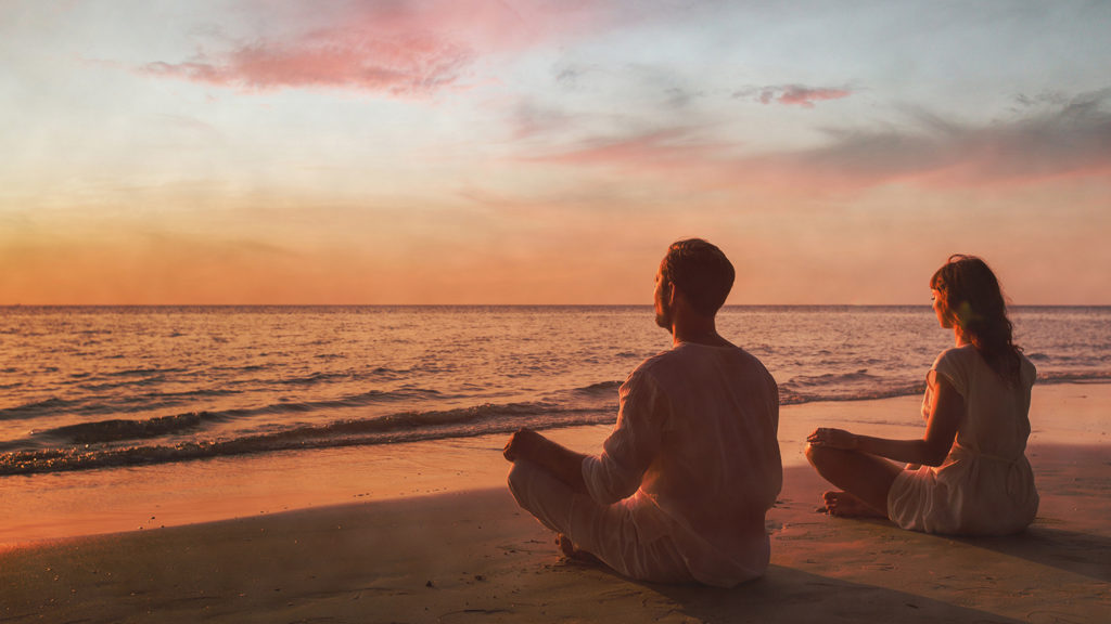 Royalty-Free Stock Photo: Couple doing yoga on the beach at sunset. 