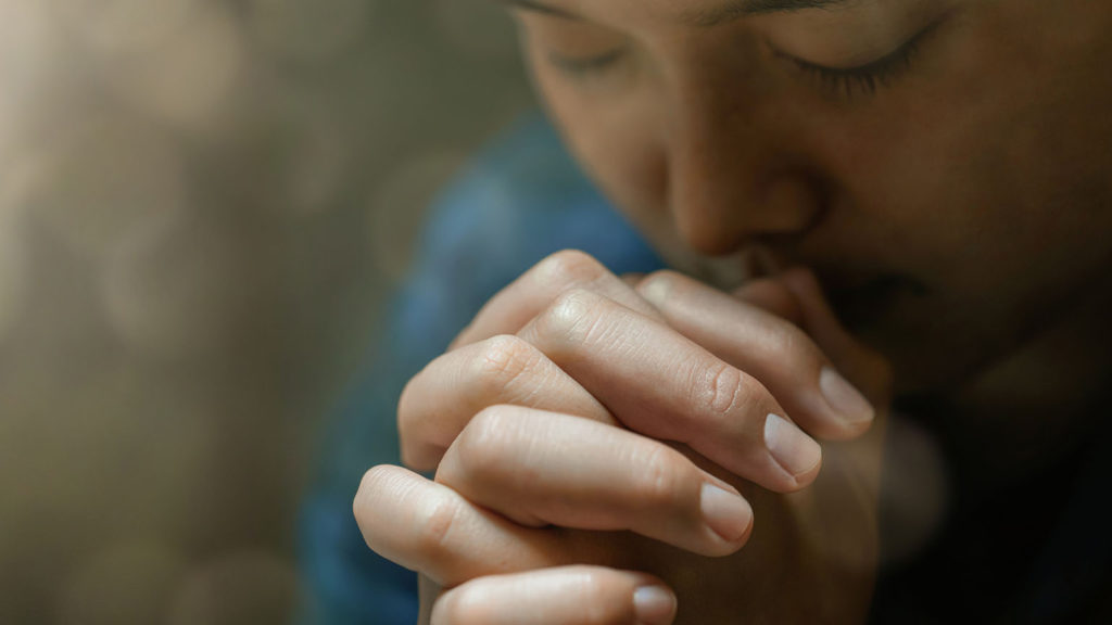 A woman prays with folded hands to let God cultivate peace in her life.