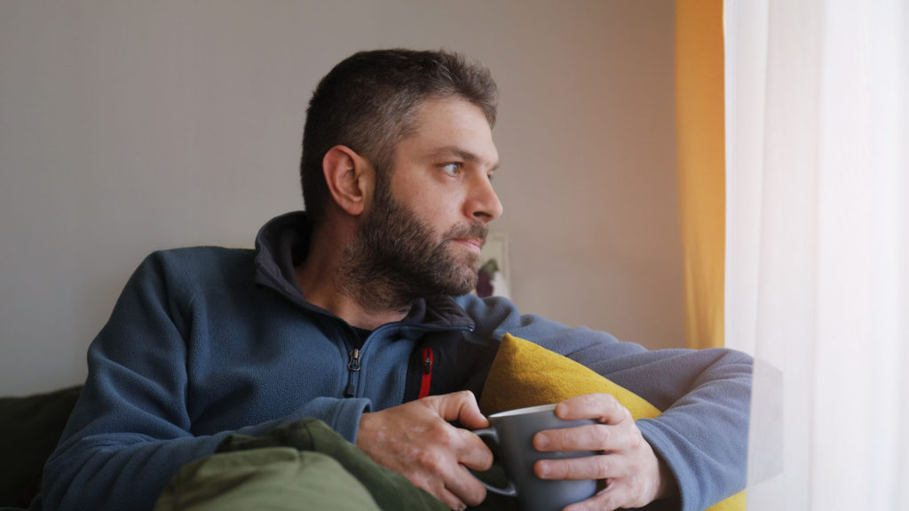 A bearded man pauses with a cup of coffee as he looks out the window and contemplates reacting with the fruit of the Spirit.