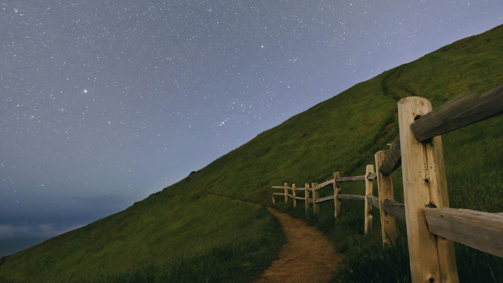 A fence lines trail on a green hill under a starlit sky shows us the secret to rest on God's mighty power.