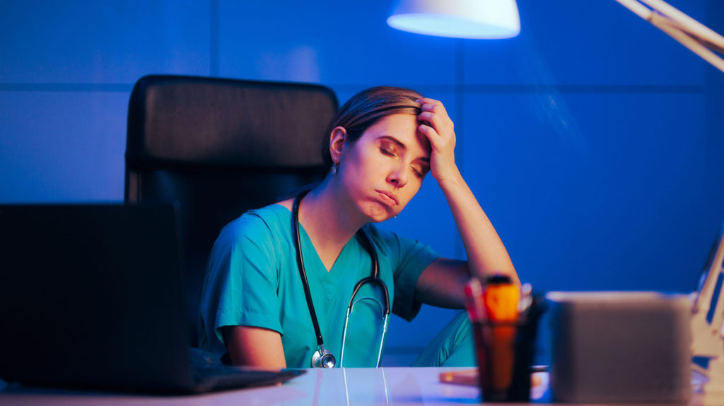 A tired nurse sitting at a desk at night closes her eyes hoping that her shift work and sleep won't be disrupted again.