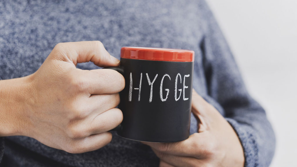 A man sips coffee from a cup with the word hygge written in it showing a sleep habit from around the world.