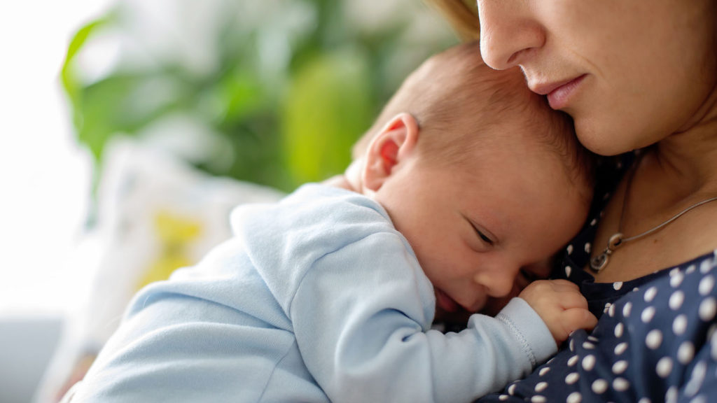 A new mom cuddles with her newborn baby as she learns the importance of sleep recovery.