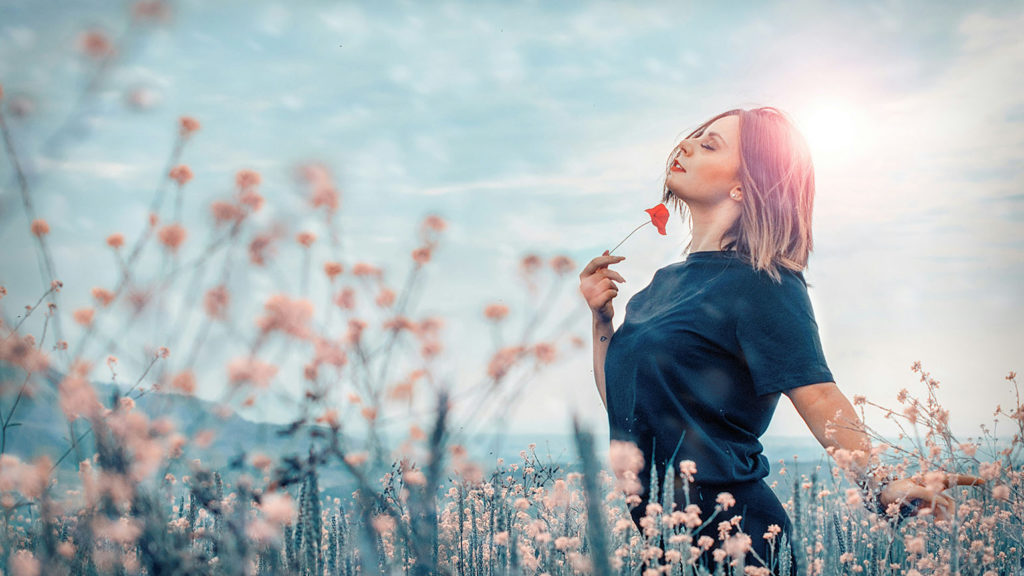 A young woman strolls peacefully through a field of pink flowers as she experiences stress relief.