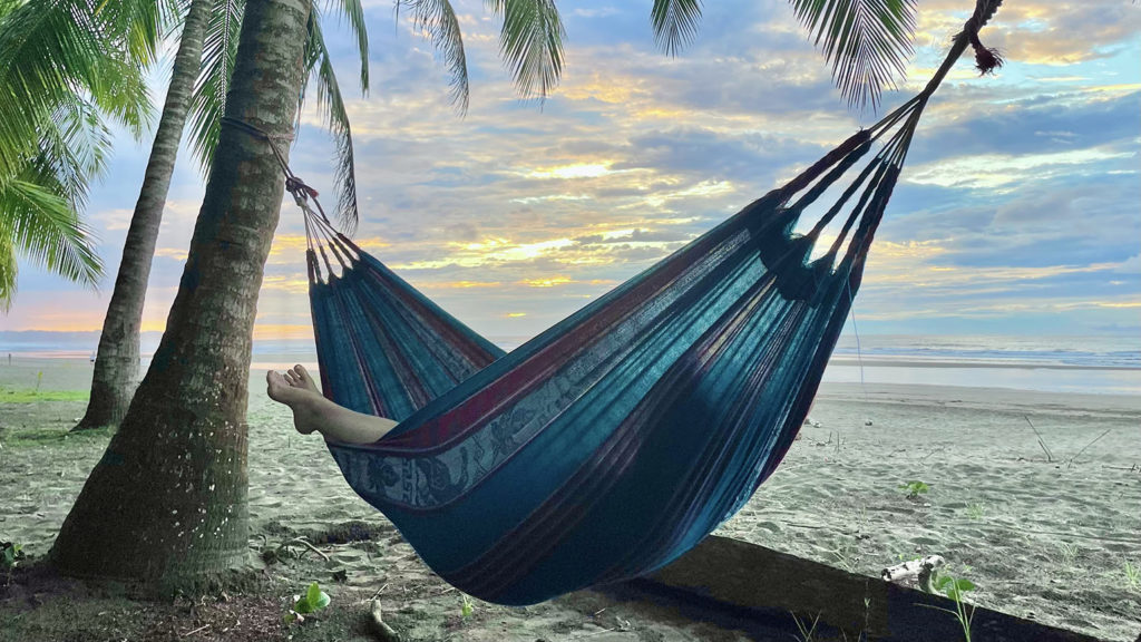 A woman sleeps in a hammock under palm trees on the beach at sunset as she has learned the secret of stree-relief sleep.