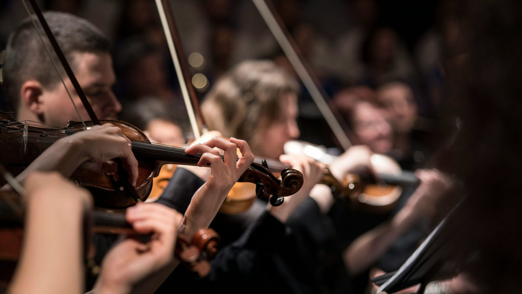 Members of an orchestra play their violins helping people witness God through music.