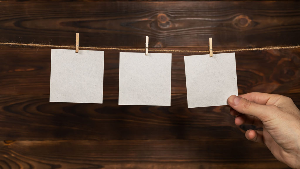 A man's hand holds a piece of clipped to a piece of twine on a wooden board as one prayer board idea.