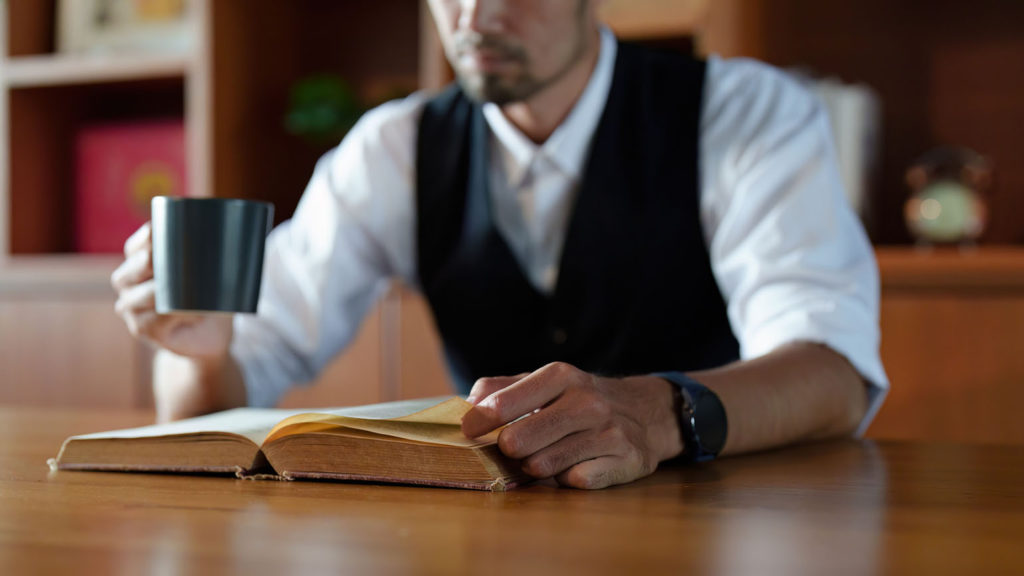 A businessman drinks coffee at a hotel table while reading his Bible knowing that travel and sleeping well need God to work.